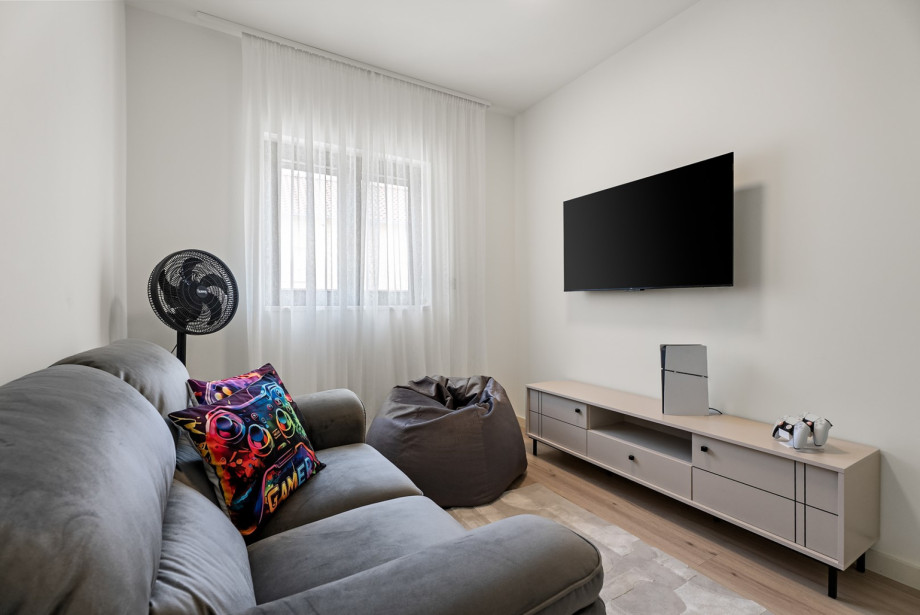 A game room with a fan, smart TV, sofa and PlayStation 5