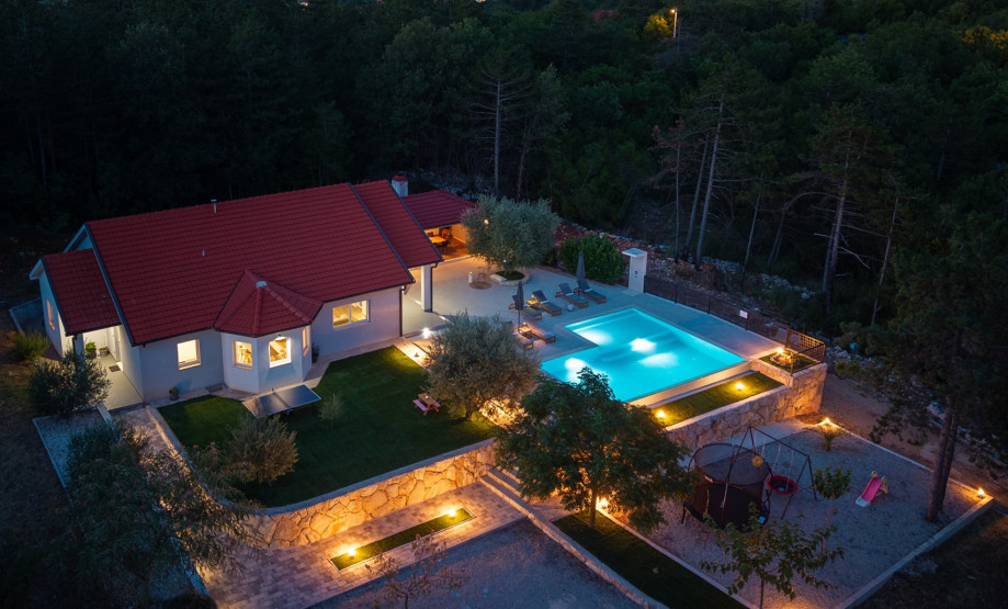 An aerial view shows the 250 sqm villa, the expansive pool, and a grassy plot with a swing and slide for children.