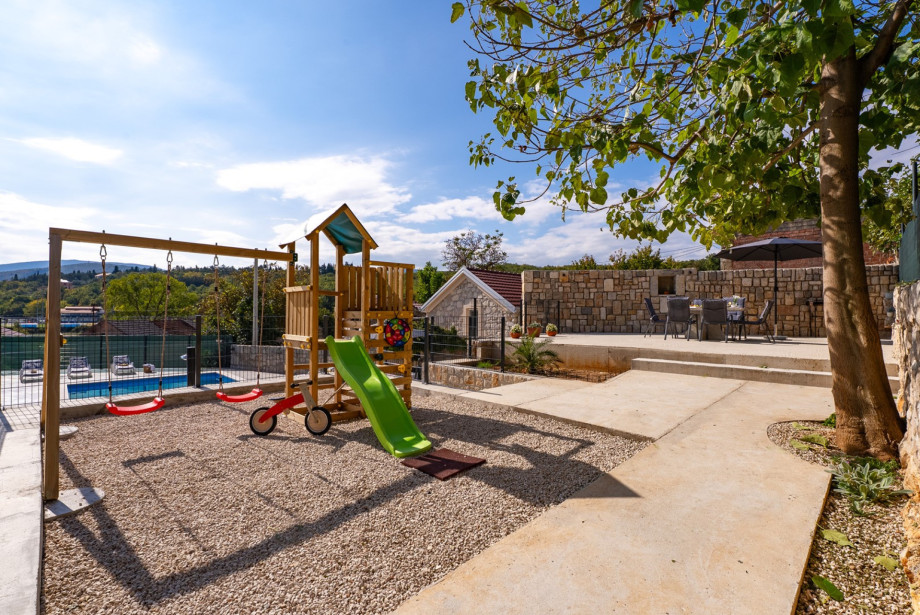The kids' climbing frame with a slide and swing is nestled beneath a tree, offering a fun-filled space for the younger guests.