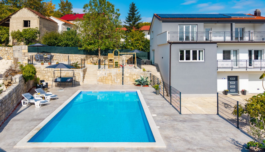 The modern villa, featuring a fully air-conditioned living space, connects seamlessly to the pool area, elevated sun deck, and kids' playground.